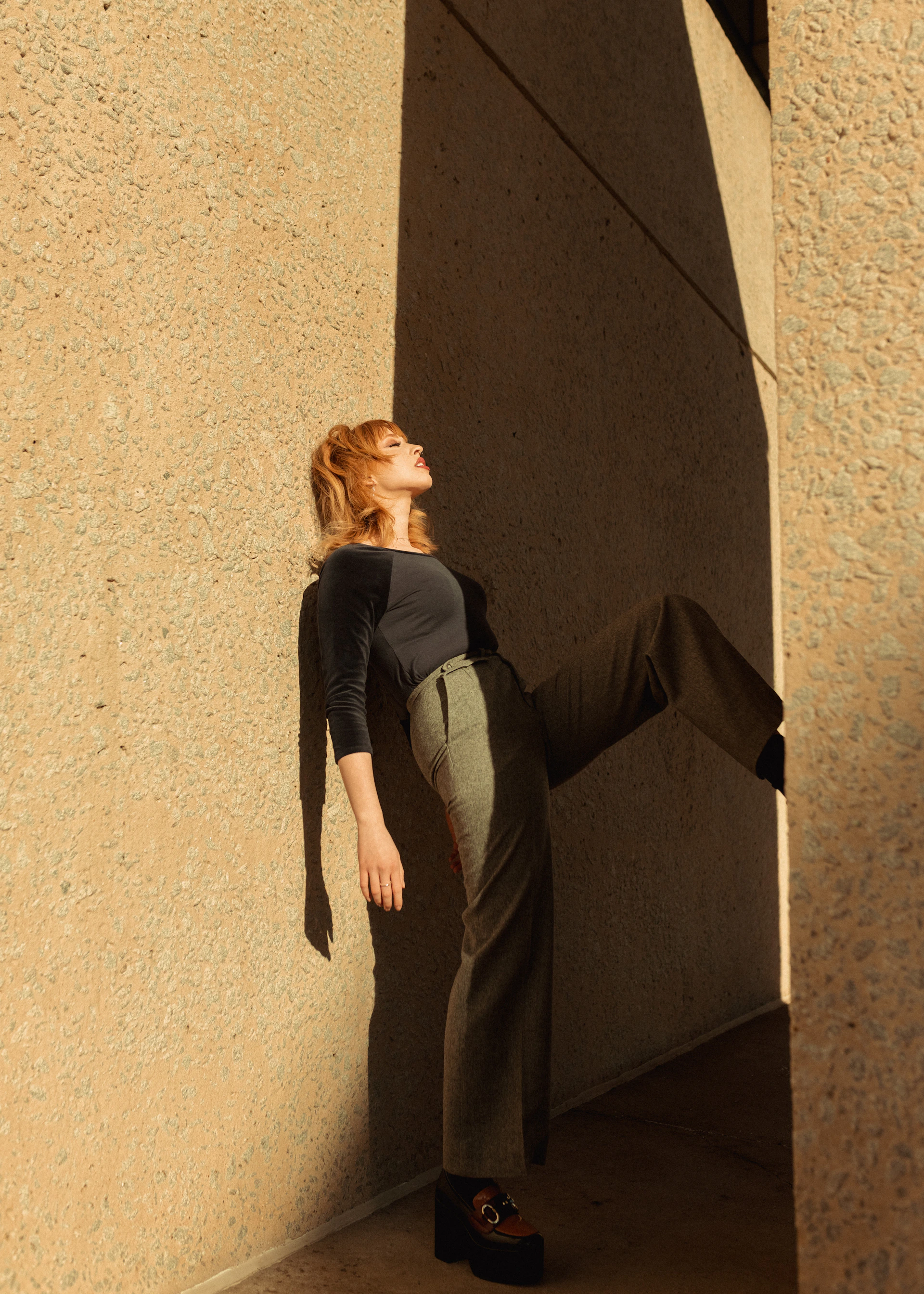 a woman leaning against a wall with her legs crossed