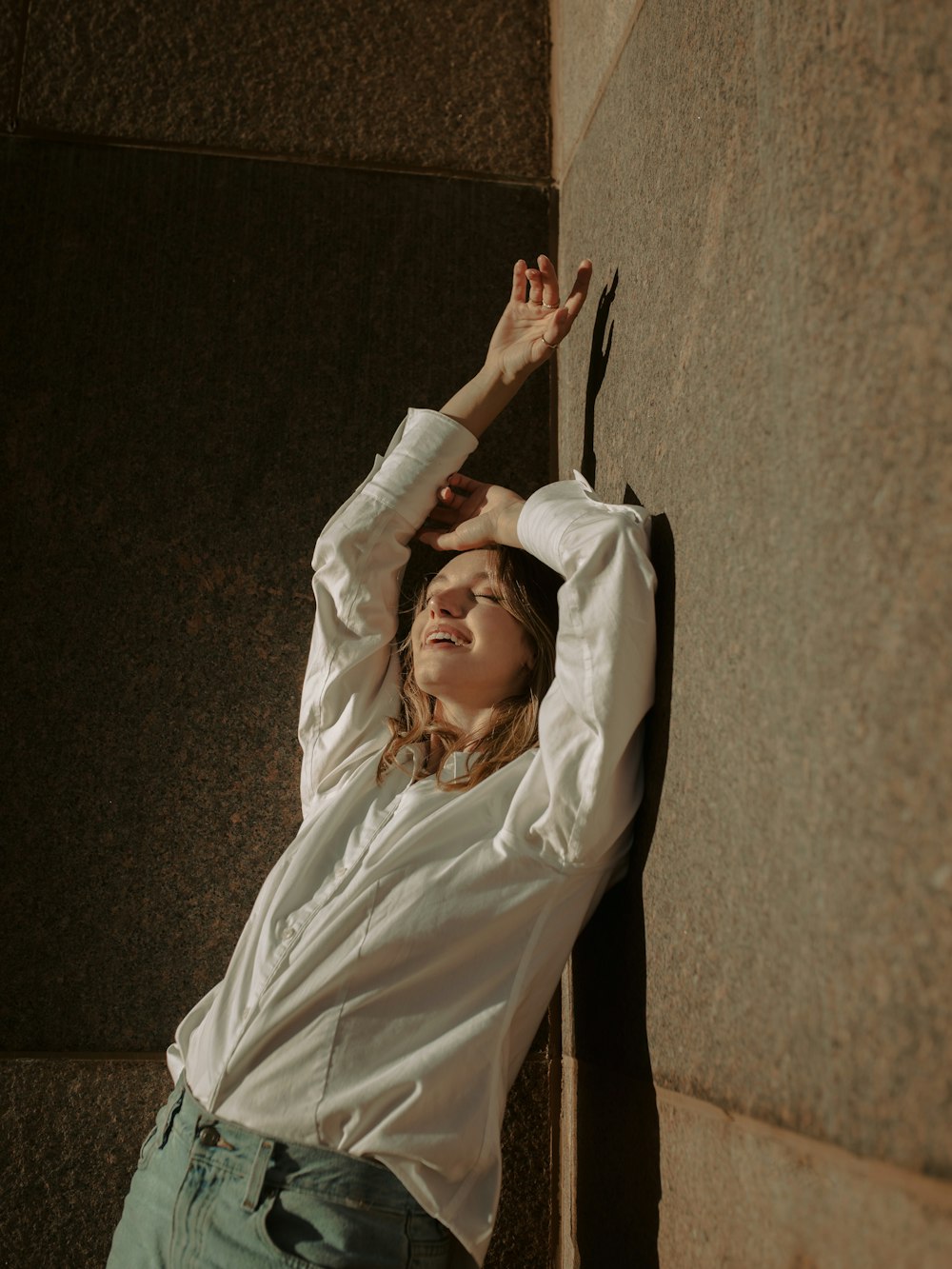 a woman leaning up against a wall with her hands in the air