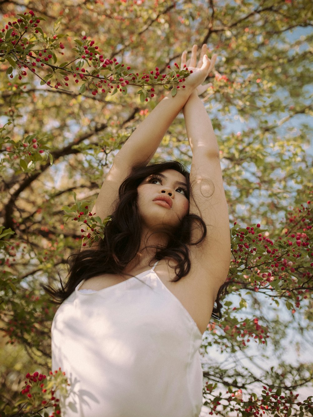 a woman in a white dress reaching up into a tree