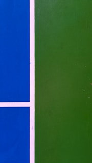 A close-up view of a sports court with a bright blue section on the left and a green section on the right, separated by white lines.