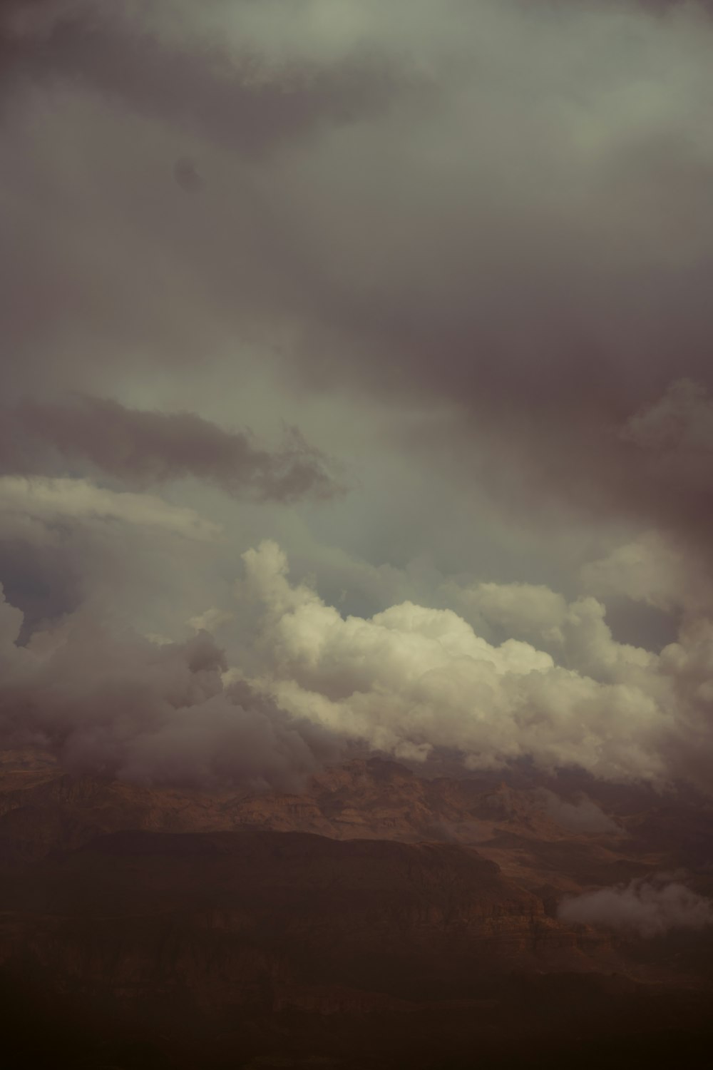 a plane flying through a cloudy sky with mountains in the background