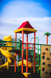 Children climbing and sliding down a colorful indoor play structure under bright purple and yellow lighting