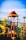A vibrant playground structure featuring a spiral slide, climbing wall, and various play equipment. The bright colors are highlighted under a clear blue sky, with distinctive reds, yellows, and greens making up the play area.
