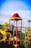 A vibrant playground structure featuring a spiral slide, climbing wall, and various play equipment. The bright colors are highlighted under a clear blue sky, with distinctive reds, yellows, and greens making up the play area.