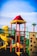 A vibrant playground structure featuring a spiral slide, climbing wall, and various play equipment. The bright colors are highlighted under a clear blue sky, with distinctive reds, yellows, and greens making up the play area.