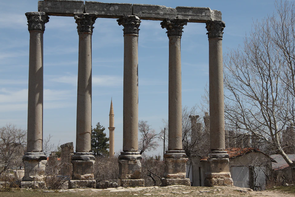 Five ancient stone columns stand tall against a clear blue sky in two rows