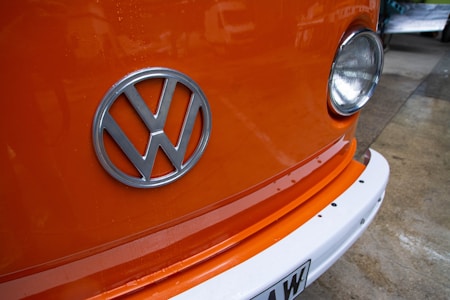 An orange vehicle with the Volkswagen logo prominently displayed on the front. The headlight on the right side of the image and a portion of the white bumper are also visible.