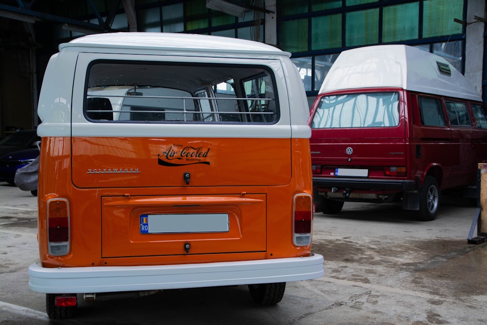 uma van laranja e branca estacionada ao lado de uma van vermelha