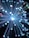 A burst of glowing fiber optic strands emitting light with varying shades, creating a vivid display of circular bokeh effects in different colors of blue, white, purple, and hints of red and green against a dark background.