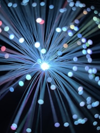 A burst of glowing fiber optic strands emitting light with varying shades, creating a vivid display of circular bokeh effects in different colors of blue, white, purple, and hints of red and green against a dark background.