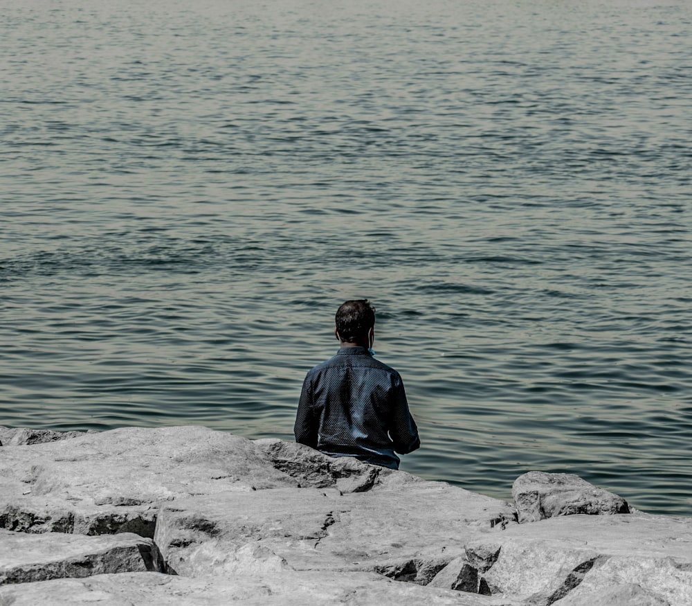 a man sitting on a rock looking out at the water