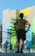 A group of people are engaged in a fitness activity outdoors. In the foreground, a man stands with his hands on his hips, facing away from the camera. In the background, other individuals are stretching or performing exercises. The setting is in front of a colorful, mural-covered building, with bright geometric patterns on the walls. A fence with decorative metalwork adds structure to the scene.