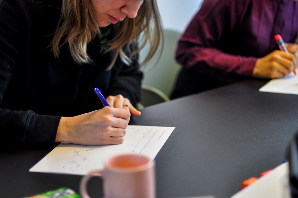 a woman sitting at a table writing on a piece of paper