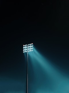 A navy blue solar lighting tower standing tall at a dark construction site, its bright white light illuminating the surroundings.