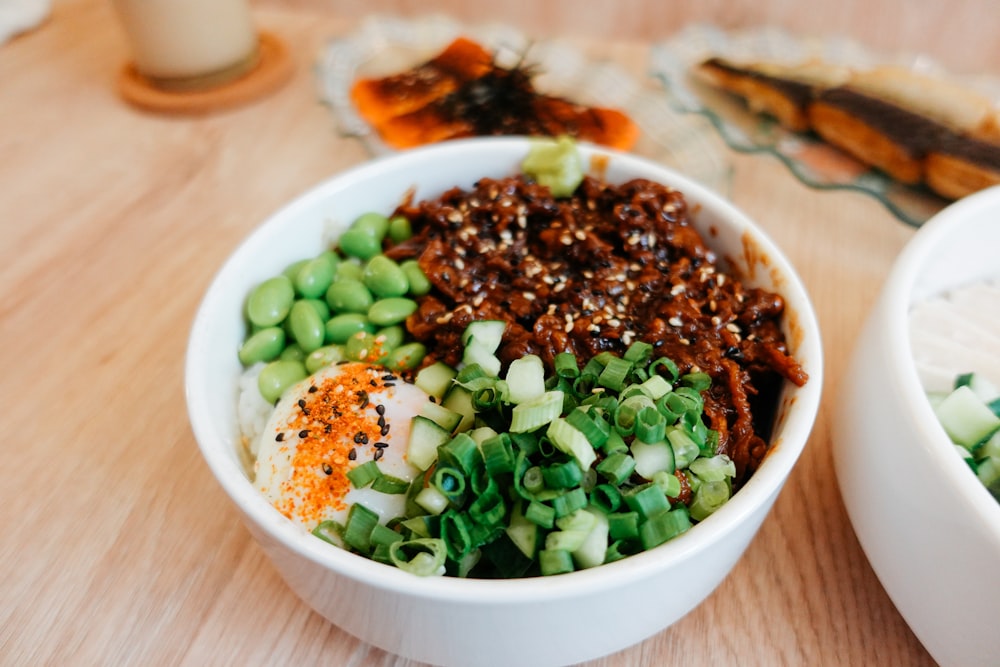 a white bowl filled with lots of food on top of a wooden table