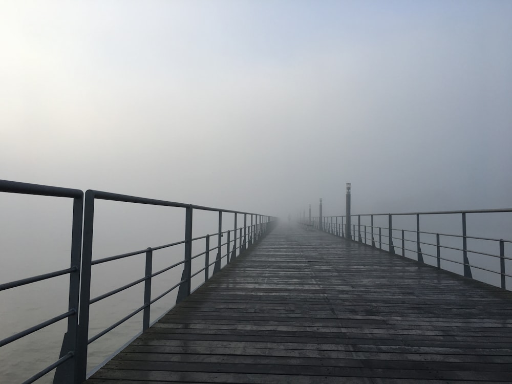 a wooden dock with a metal railing on a foggy day