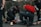 Several emergency responders attend to a person lying on the ground. One responder kneels beside the individual, holding medical equipment, while another is positioned nearby with a red medical bag. The scene suggests a medical emergency, with responders wearing uniforms and equipment indicating a professional, urgent atmosphere.