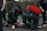 Several emergency responders attend to a person lying on the ground. One responder kneels beside the individual, holding medical equipment, while another is positioned nearby with a red medical bag. The scene suggests a medical emergency, with responders wearing uniforms and equipment indicating a professional, urgent atmosphere.