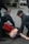 Emergency responders in uniforms are performing a training exercise with a medical mannequin on the pavement. There is a red medical bag near the mannequin, and one responder is wearing blue gloves.