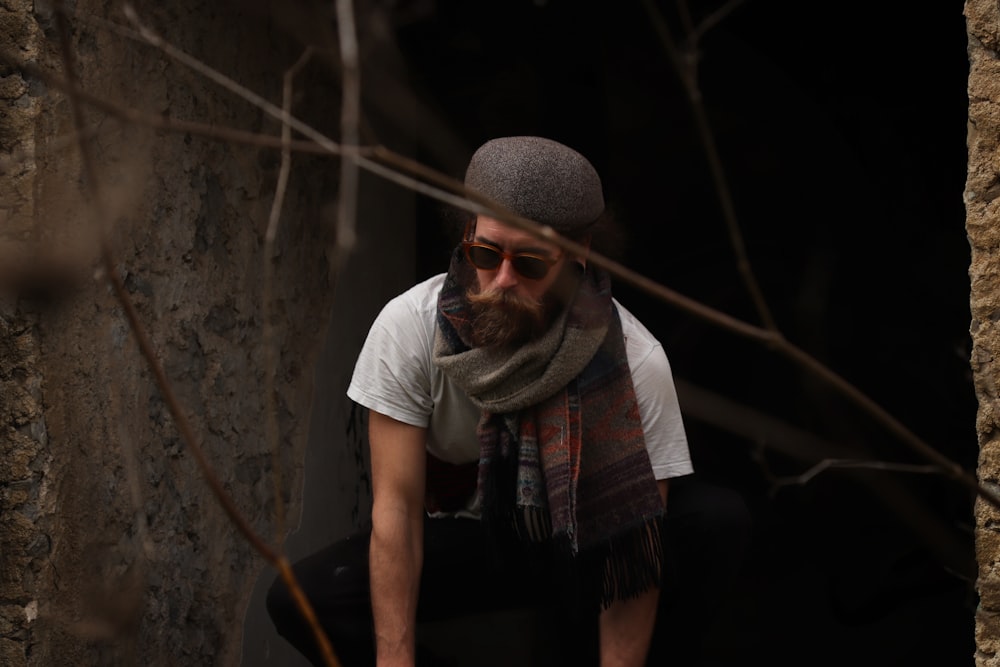 a man wearing a hat and scarf crouching down