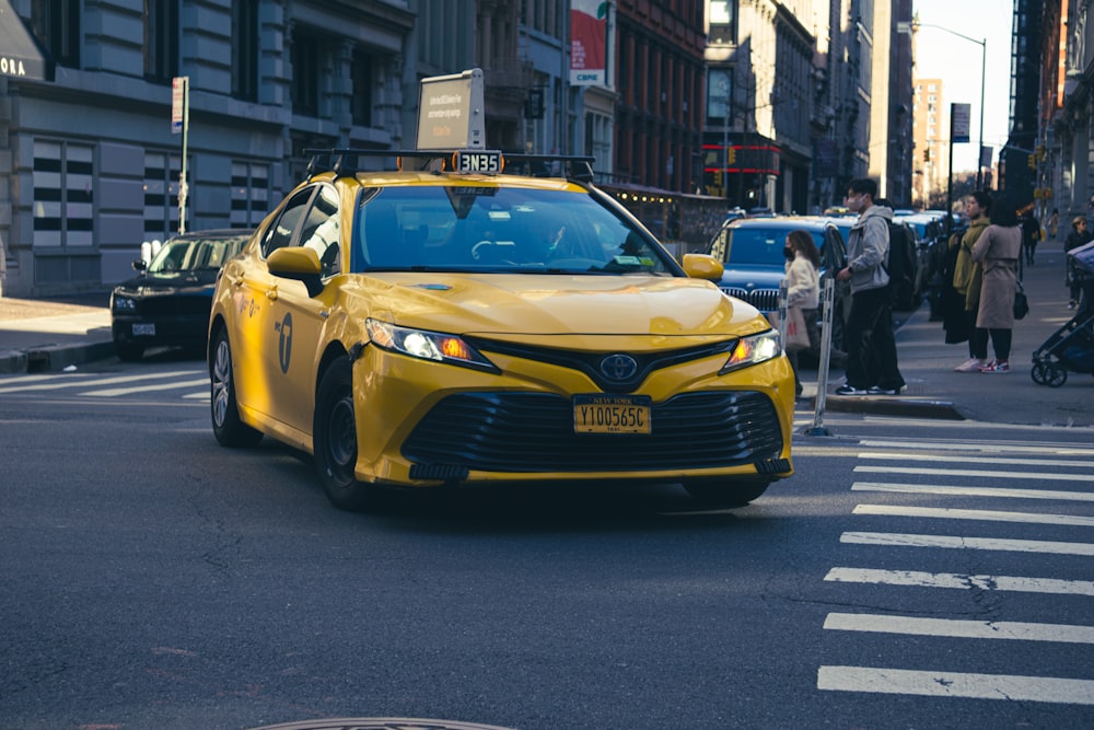 a yellow car driving down a street next to tall buildings