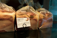Several loaves of bread are wrapped in translucent plastic bags, each with a printed label showing nutritional information and the name 'Whole Milk Loaf'. The bread is organized on a reflective surface, and the packaging has a modern design with wavy lines.