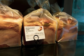 Several loaves of bread are wrapped in translucent plastic bags, each with a printed label showing nutritional information and the name 'Whole Milk Loaf'. The bread is organized on a reflective surface, and the packaging has a modern design with wavy lines.