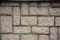 Roughly textured stone wall composed of rectangular bricks laid in a staggered pattern.