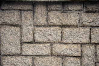 Roughly textured stone wall composed of rectangular bricks laid in a staggered pattern.