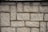 Roughly textured stone wall composed of rectangular bricks laid in a staggered pattern.
