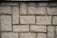 Roughly textured stone wall composed of rectangular bricks laid in a staggered pattern.