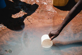 a person reaching for a plastic cup in a puddle of water