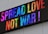 A digital sign displaying the phrase 'Spread Love, Not War!' in vibrant, colorful letters. The text is arranged in multiple colors against a white background, creating a bright and positive visual effect.