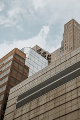 A cluster of modern skyscrapers with various geometric designs and reflective surfaces against a cloudy sky.