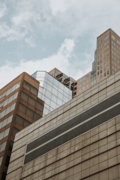 A cluster of modern skyscrapers with various geometric designs and reflective surfaces against a cloudy sky.