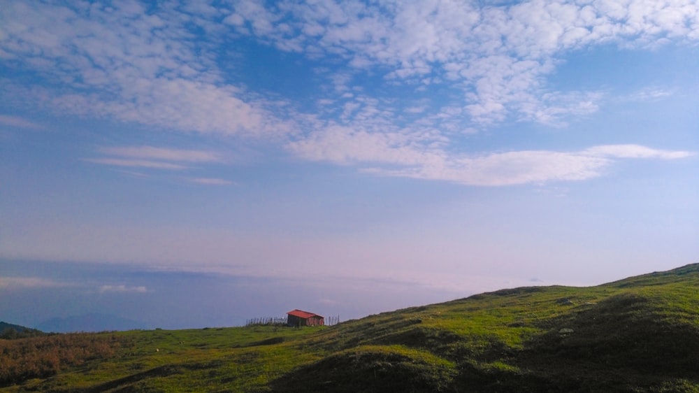 a lone house on a grassy hill under a blue sky