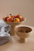 A collection of bright stoneware bowls filled with fresh fruits on a simple linen cloth.