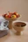 Close-up of a colorful stoneware bowl holding fresh fruit on a rustic wooden table, surrounded by soft textiles.