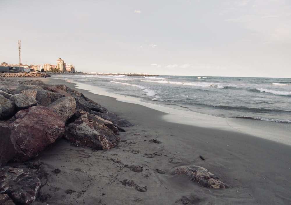 a beach with rocks and water and buildings in the background