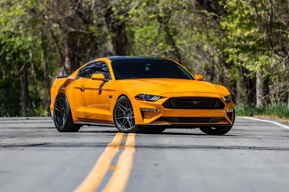 a yellow ford mustang on a road with trees in the background