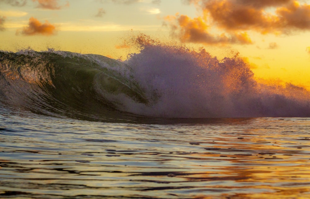 the sun is setting behind a large wave