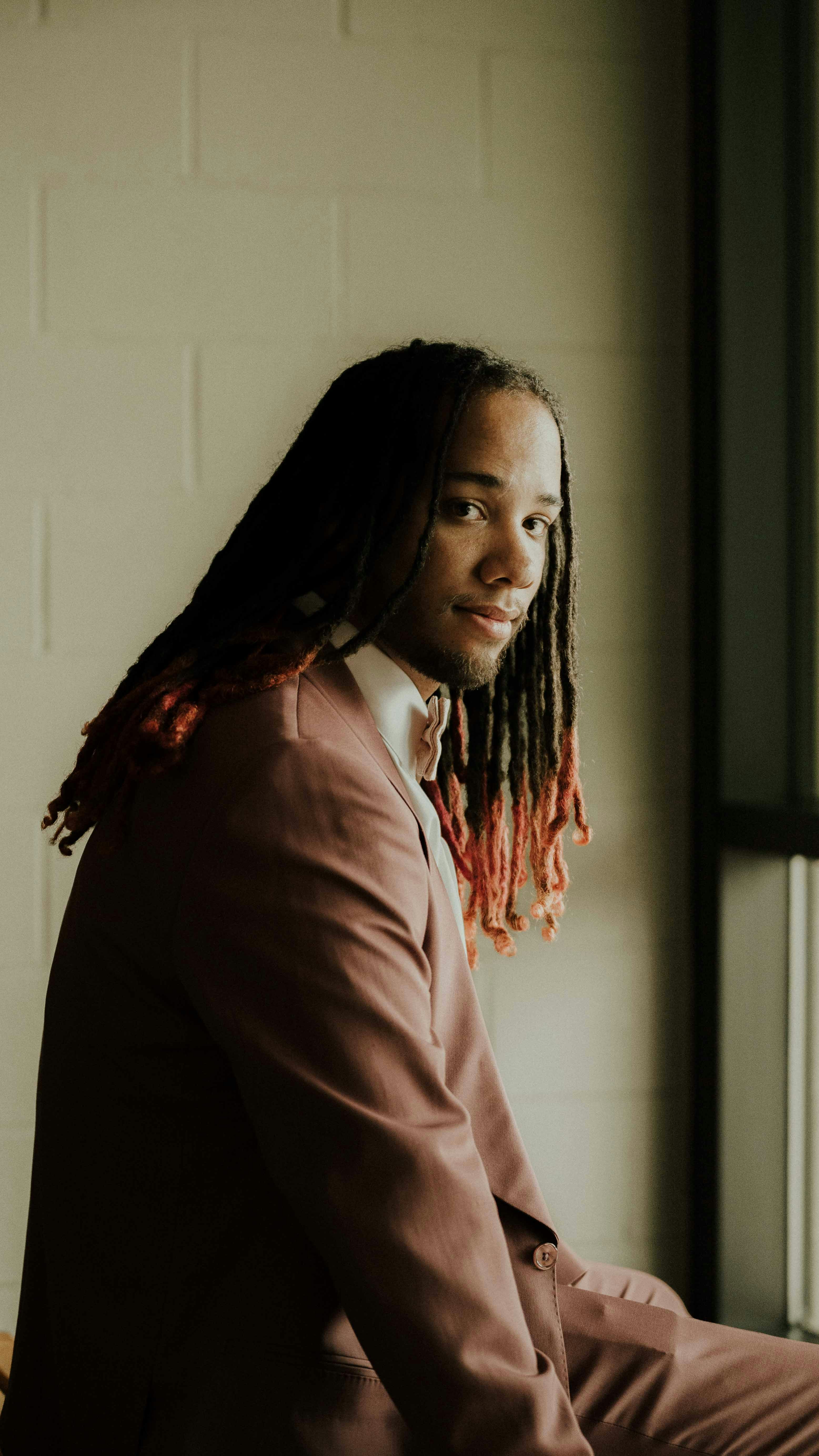 a man with dreadlocks sitting in front of a window
