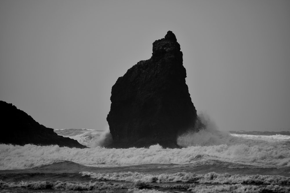 a black and white photo of a rock in the ocean