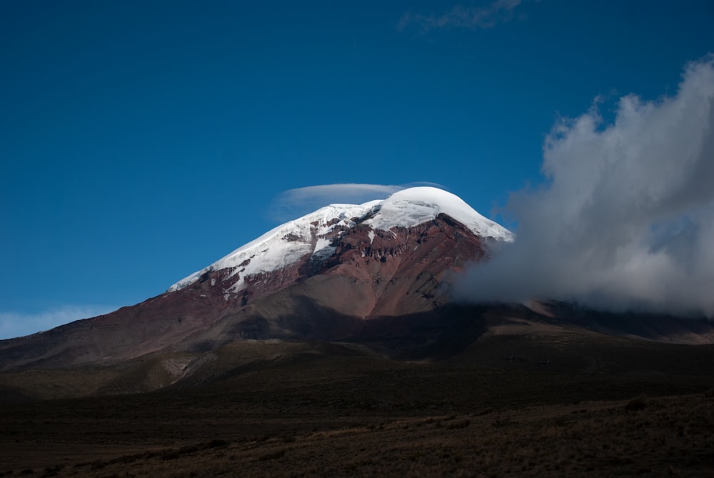 uma montanha coberta de neve com uma nuvem no céu