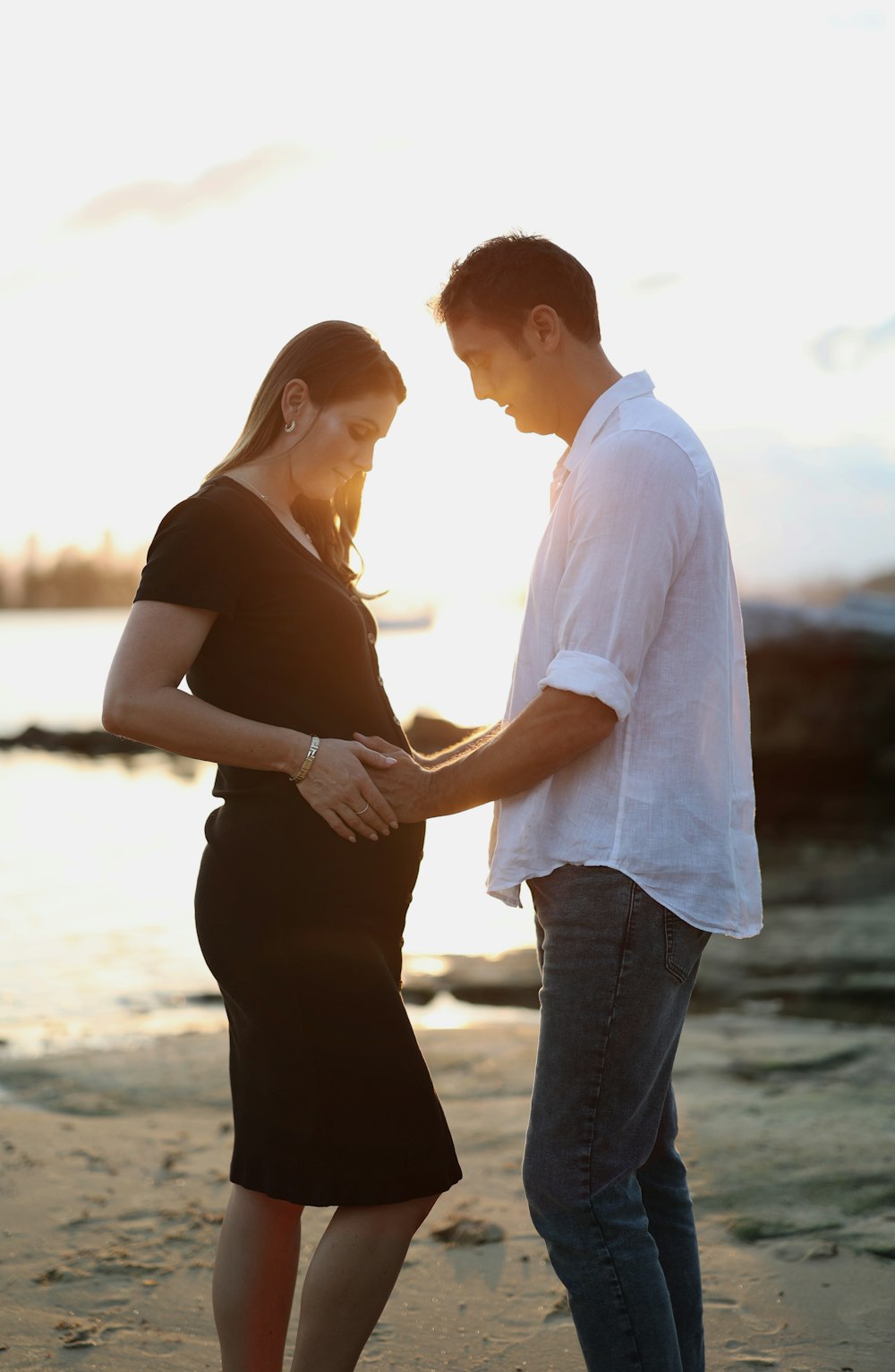 a pregnant couple standing on the beach at sunset