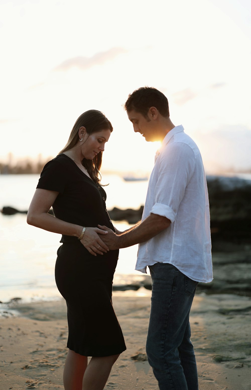 a pregnant woman standing next to a man on a beach