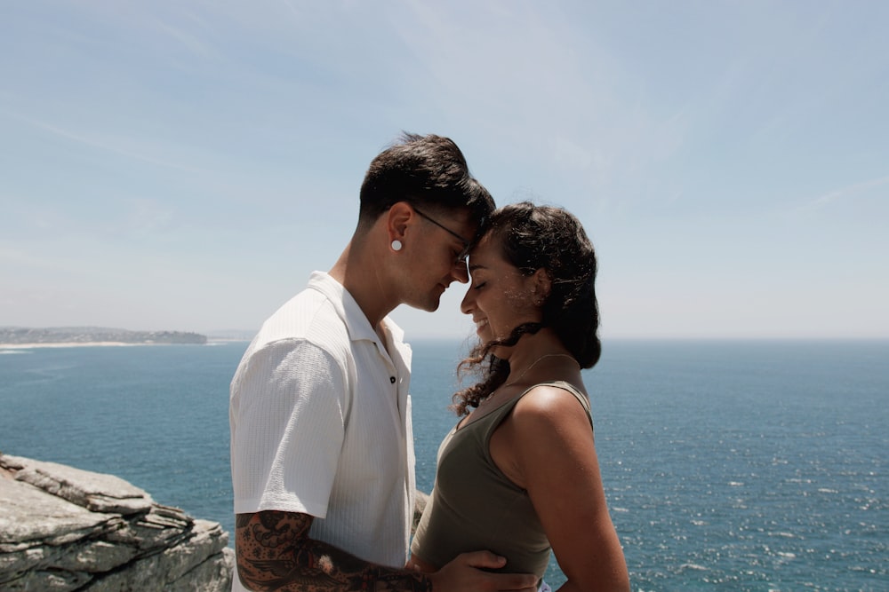 a man and woman standing next to each other near the ocean