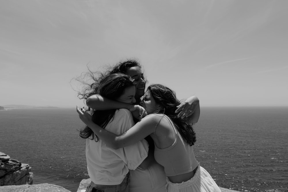 a group of women hugging each other on top of a cliff