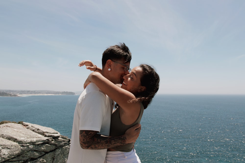 a man and a woman embracing on a cliff overlooking the ocean