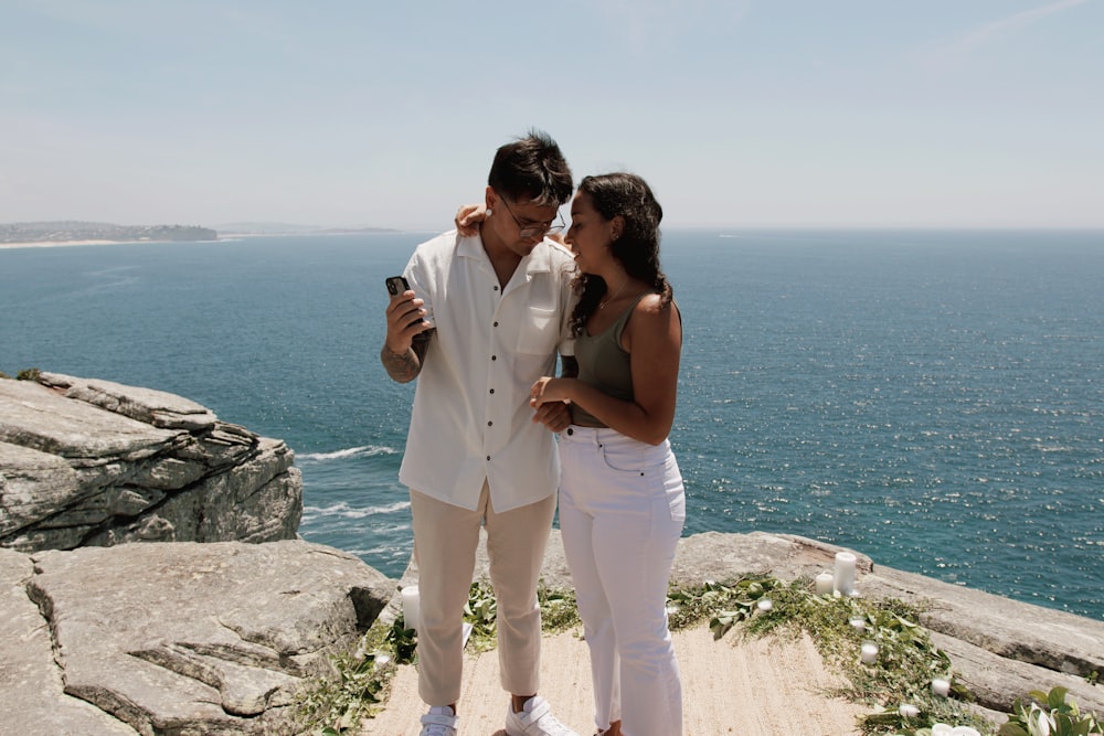 Un hombre y una mujer parados en la cima de un acantilado junto al océano